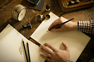 A person writing on a note pad with pencils scattered around and a clock showing the time