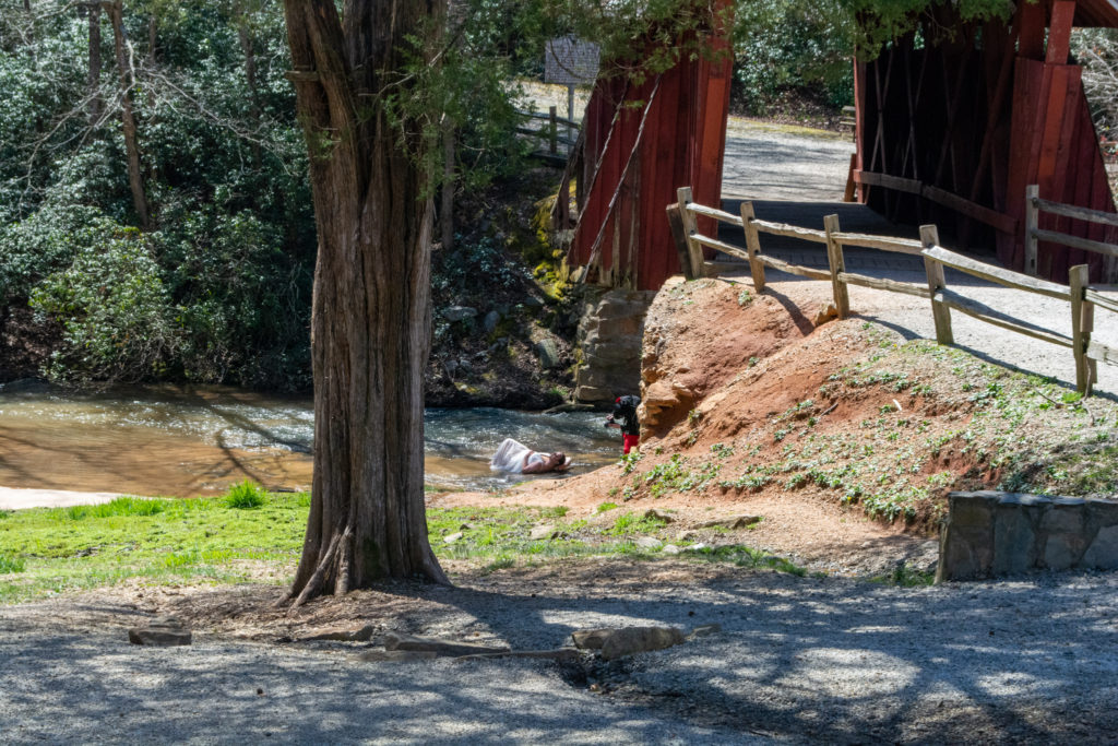 A photographer taking pictures of a model lying in the river beneath a covered bridge