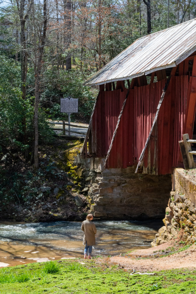 A woman standing below an old covered bridge